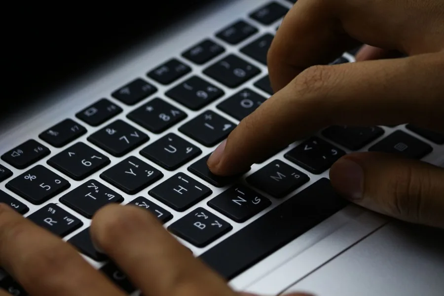 Prim-plan cu mâini care tastează pe tastatura unui laptop, în lumină slabă.